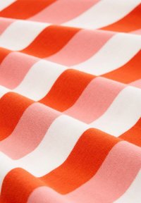 Pruhovaná látka s vlnitými liniemi v oranžové, růžové a bílé barvě. Měkká textura s hladkým povrchem, která ukazuje střídající se barvy v opakujícím se vzoru.