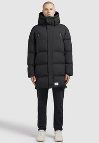 Svart puffjacka med hög krage, framfickor med dragkedja och en logotyp-plåster. Mjuk textur och vadderad design för isolering.