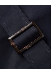 Correa de tela azul marino con una hebilla rectangular marrón oscuro y brillante que presenta el texto grabado "TOMMY HILFIGER". Textura suave y costuras apretadas.