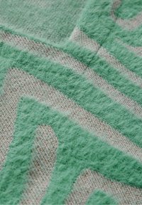 Tissu texturé présentant un motif géométrique aux couleurs vert menthe et gris clair. La section vert menthe est duveteuse, contrastant avec un fond lisse.