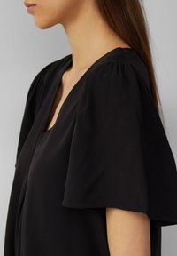 Blusa nera con scollatura a V, maniche corte a sbuffo e una texture morbida e liscia. Il design è semplice ed elegante.