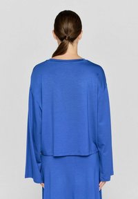 Blå langærmet top lavet af blødt stof, med en afslappet pasform og rund halsudskæring, samt en cropped kant der sidder ved taljen.