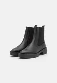 Botas de cuero negras hasta el tobillo con un acabado suave, paneles elásticos en los laterales y una suela gruesa de goma negra. Diseño de punta afilada y tiradores.