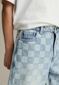 Lichtblauwe geruite denim shorts met een hoge taille, vijf zakken en een knoopsluiting aan de voorkant. De stof heeft een vervaagde textuur.