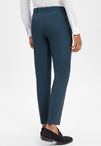 Maßgeschneiderte türkisfarbene Hosen aus strukturiertem Stoff. Bieten eine schmale Passform, Gesäßtaschen und einen mittelhohen Bund, kombiniert mit dunklen Mokassins.