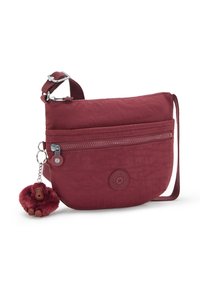 Mörk röd nylon crossbody-väska med en dragkedjeförsedd framficka, justerbar rem och en nyckelring med en brun plyschapa.
