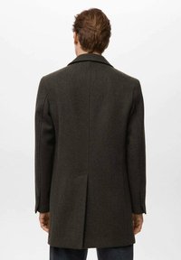 Abrigo de lana marrón oscuro con solapa con muesca, abertura trasera y hombreras estructuradas. Presenta un corte entallado y tejido texturizado.