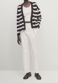 Granatowy i kremowy kardigan w paski, krótki, z głębokim dekoltem w serek i guzikami. Noszony na białym topie na ramiączkach, zestawiony z białymi spodniami o wysokim stanie.