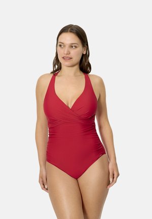 Mujer con un traje de baño rojo de una pieza, con cuello halter y cintura fruncida, de pie y mirando ligeramente hacia su izquierda.