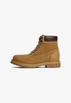 Bottines lacées en cuir tan avec un col rembourré marron foncé et une semelle robuste, logo sur le côté estampillé "Tommy Hilfiger."