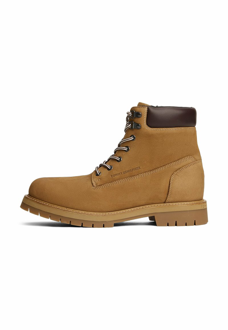 Botín de cuero marrón claro con cordones, cuello acolchado en marrón oscuro y suela robusta, logo lateral estampado "Tommy Hilfiger."