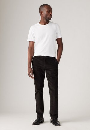 Witte crew-neck t-shirt, zwarte corduroy broek en zwarte schoenen. De outfit is eenvoudig en goed passend, met een neutrale kleurenpalet.