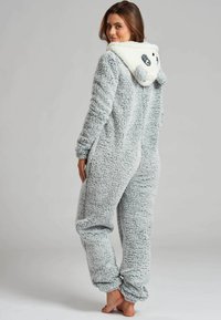 Tutina grigia e fluffy con texture morbida, dotata di cappuccio a tema panda, orecchie tonde e dettagli facciali in bianco e nero.