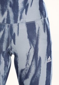 Navyja i svijetloplave atletske tajice imaju teksturirani, apstraktni uzorak, ravne šavove i mali bijeli Adidas logo na donjem dijelu noge.