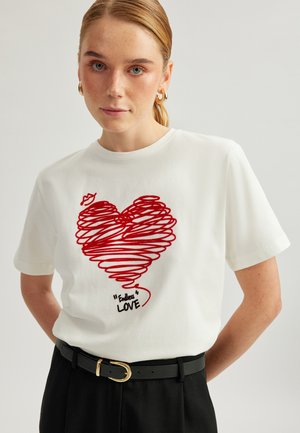 White t-shirt with short sleeves featuring a red spiral heart design and the text “Endless Love” in black, worn with a black belt.