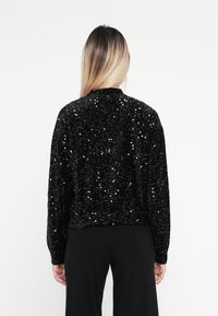 Czarna kurtka z cekinami, z okrągłym kołnierzem, długimi rękawami i teksturowaną powierzchnią. Posiada dopasowaną talię, co zapewnia zorganizowaną sylwetkę.