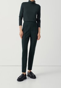 Ciemnozielony golf zestawiony z dopasowanymi spodniami z przodu z plisami. Czarne buty wsuwane na grubych podeszwach dopełniają całość.