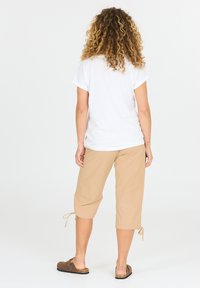 Beige cropped-housut, joissa on nyörikohdat helmassa, yhdistettynä osaavaan valkoiseen t-paitaan ja ruskeisiin puukenkihin, nähtynä takaa.