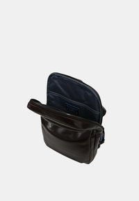 Bolso mensajero de cuero marrón con cierre de cremallera. El interior presenta un forro oscuro y un bolsillo deslizante. Textura suave y diseño compacto.