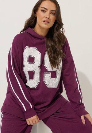 Felpa viola con dettagli a strisce bianche, caratterizzata da una grande grafica "89" in stile usurato. Vestibilità oversize, materiale misto cotone, polsini a costine.