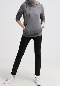 Harmaa huppari, jossa on kaulukseen kietoutuva hupunauha ja etutaskut, yhdistettynä mustiin kapealanteisiin farkkuihin ja valkoisiin tennareihin, joissa on vihreitä yksityiskohtia.