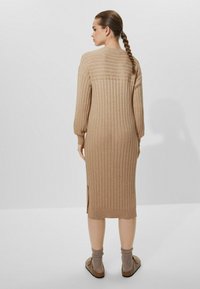 Robe midi en tricot beige clair avec une texture à côtes verticales, manches longues, fentes sur les côtés et un col rond, associée à des chaussures brunes à enfiler.