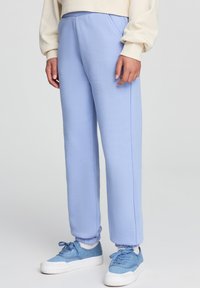 Pantaloni sportivi azzurri con elastico in vita, tasche laterali e orli a costina, realizzati in tessuto morbido, abbinati a sneakers blu.