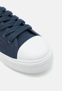 Baskets en toile bleu marine avec bout en caoutchouc blanc, semelle texturée blanche et lacets plats, dotées de coutures renforcées sur la tige.
