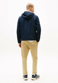Chaqueta navy con capucha, material ligero y mangas largas, combinada con pantalones beiges y zapatillas con un diseño estampado.