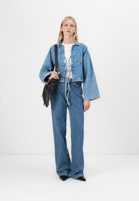 Ieskrūdēts denim džinsusām, ar platām piedurknēm, apvienots ar augsto vidukli ziliem džinsiem. Modelis tur melnu frēnu rokassomu. Vēl zemā T-krekls.