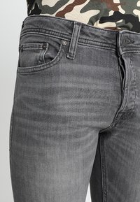 Szare dżinsy z denimu o dopasowanym kroju, z pięcioma kieszeniami i metalowymi elementami. Charakteryzują się delikatnym wyblaknięciem i gładką teksturą.