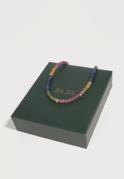 Πολύχρωμο κολιέ με χάντρες τοποθετημένο σε σκούρο πράσινο κουτί με χρυσό λογότυπο "JIA JIA" σε λευκό φόντο.