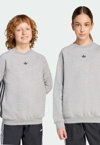 Sivý mikina s raglánovými rukávmi, čierny vyšívaný logo na hrudi, ribbované manžety a lem, skombinovaná s čiernymi nohavicami s tromi pruhmi.