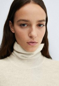 Pletena turtleneck pulover u svijetlo krem boji, s teksturiranim uzorkom i uskim dizajnom oko vrata.