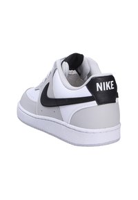 White and gray athletic sneaker with leather and synthetic material, rounded toe, black Nike logo on side and heel, and textured sole.