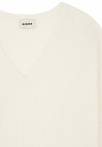 Weißer V-Ausschnitt-Pullover aus strukturiertem, gestricktem Stoff. Mit dezenten Mustern und einem Etikett mit der Aufschrift "RODIER" am Halsausschnitt.