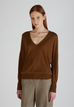 Brązowy sweter w serek z miękkiego materiału dzianinowego, z długimi rękawami, ściągaczami i luźnym krojem, połączony z w kratę spodniami.