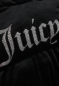 Tessuto in velluto nero con la parola "Juicy" in grandi strass argento disposti in un font ornato sulla parte anteriore.
