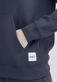 Tamsiai pilka sportinė maikė su priekinėmis kišenėmis, apsiūtomis rankovėmis ir balta etikete su "NORTH BEND" logotipu. Minkšta medžiaga su glotniu paviršiumi.