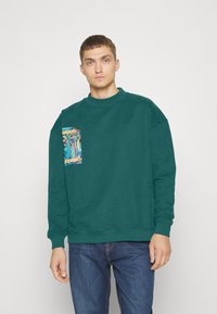 Groene sweatshirt van katoenmixstof, met een kleurrijk grafisch pocketontwerp. Geribbelde manchetten en zoom, losse pasvorm.