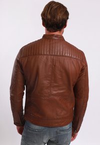 Braune Lederjacke mit gesteppter Schulterverarbeitung, slim fit und seitlichen Reißverschlüssen. Glatte Textur, flacher Kragen und minimalistisches Design.