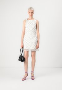 Vestido blanco sin mangas con un patrón entrecruzado, tela texturizada y una silueta ajustada. Combinado con un bolso negro y tacones morados de tiras.