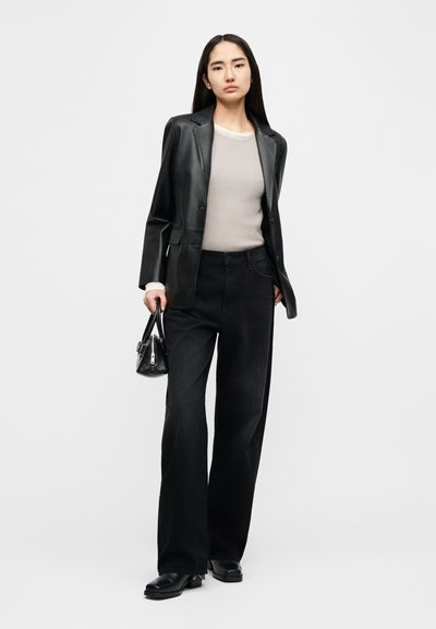 Μαύρο δερμάτινο σακάκι πάνω από μπεζ ριμπ πουλόβερ, σετ με ψηλόμεσα μαύρα τζιν παντελόνια και μικρή μαύρη τσάντα. Λείες υφές.