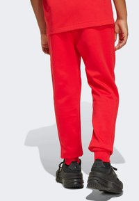 Röda bomullsbyxor med smalnade ben, med elastisk midja och sidofickor, tillsammans med svarta träningsskor.