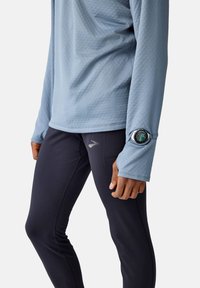 Himmelblaues, langärmliges Sportshirt aus strukturierter Stoff mit Daumenlöchern, kombiniert mit schwarzen, enganliegenden Leggings mit einer Nahttasche und Logo.