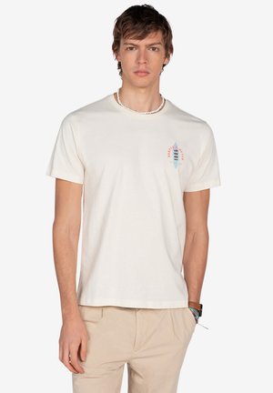 Camiseta de algodón color crema con mangas cortas, que presenta un gráfico estilizado de una tabla de surf en azul y rojo en la parte izquierda del pecho.
