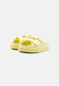 Sandales jaunes avec de larges brides élastiques, semelle en caoutchouc texturée, forme arrondie et design ouvert au niveau des orteils ; légères et décontractées.