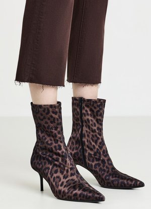 Knöchelhohe Stiefel mit spitzer Spitze, Leopardenmuster und seitlichen Reißverschlüssen, getragen zu braunen, gekürzten Hosen mit ausgefransten Säumen.