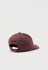 Casquette de baseball marron foncé avec une broderie noire "BOSS" sur la sangle arrière réglable, présentée sur un fond blanc uni.