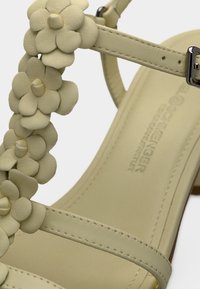 Ανοιχτοπράσινο σανδάλι με διακοσμητικά λουλούδια, απαλή υφή δερμάτινου, λεπτό σχέδιο λουριού και χαμηλό, χοντρό τακούνι.